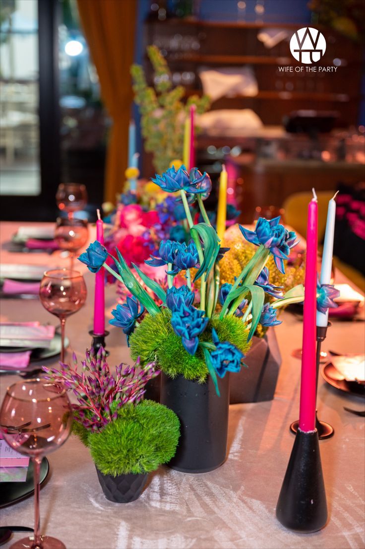 the table is set with candles and flowers in black vases on top of it