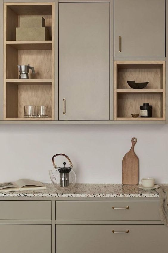 a kitchen with gray cabinets and marble counter tops, an open book shelf above the sink