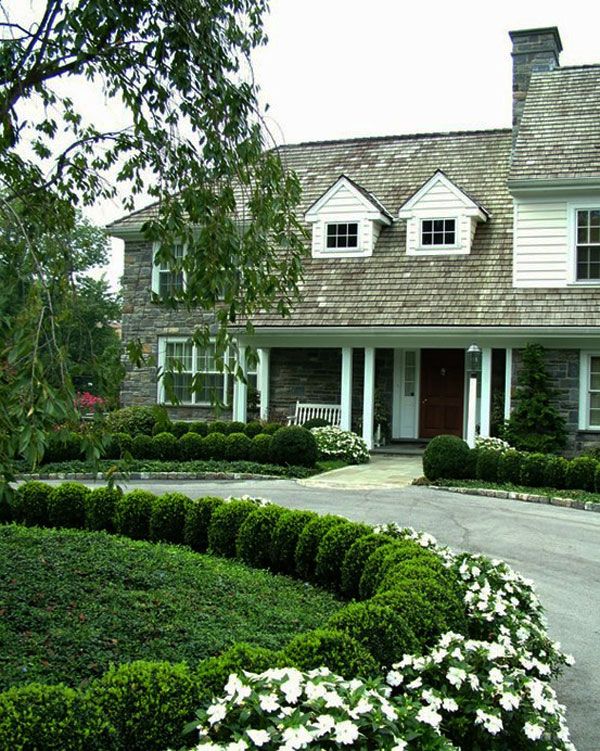 a large house with white flowers in the front yard and bushes around the driveway area