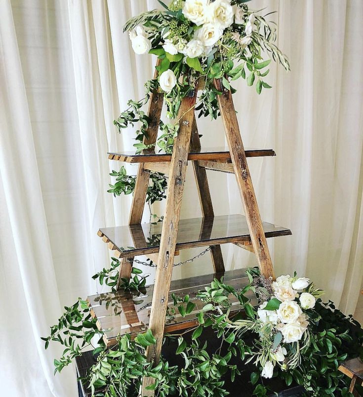 a wooden ladder decorated with white flowers and greenery for a wedding ceremony or party