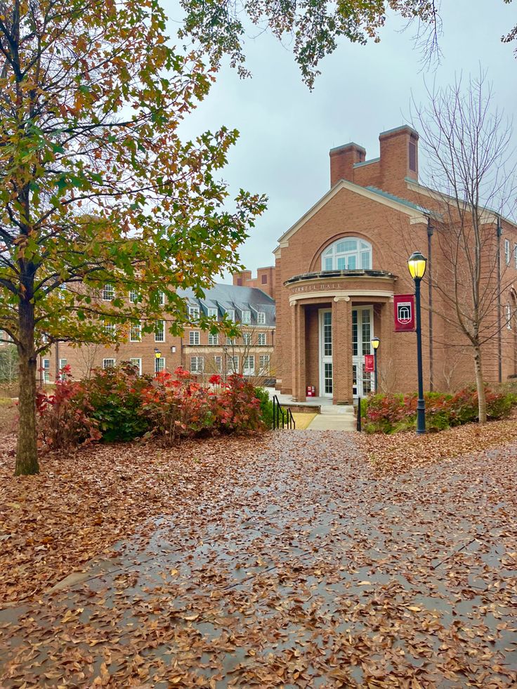 a brick building surrounded by trees and leaves on the ground with a street light in front of it