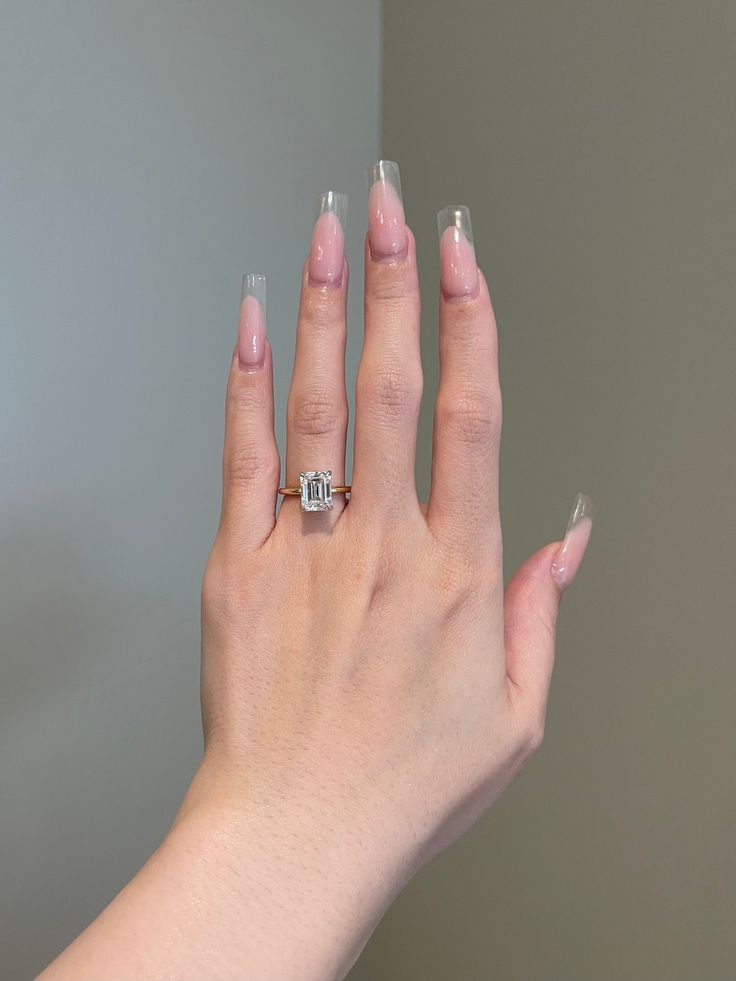 a woman's hand with pink nail polish holding an engagement ring