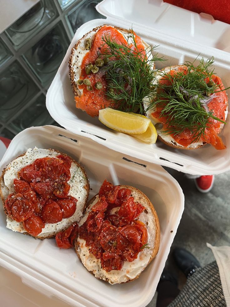 two plastic containers filled with sandwiches covered in tomato sauce and dill sprigs