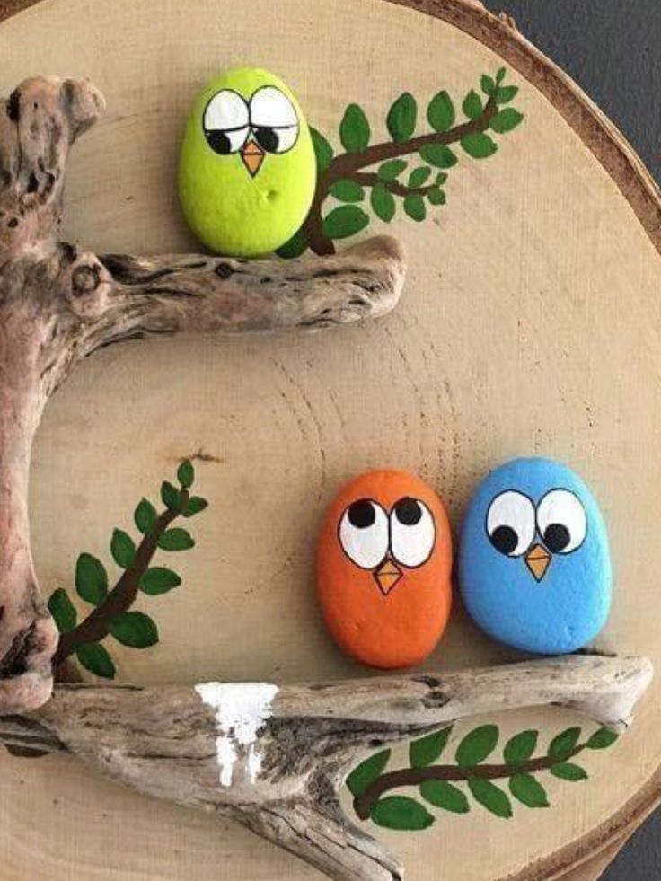 three painted rocks sitting on top of a piece of wood next to a tree branch