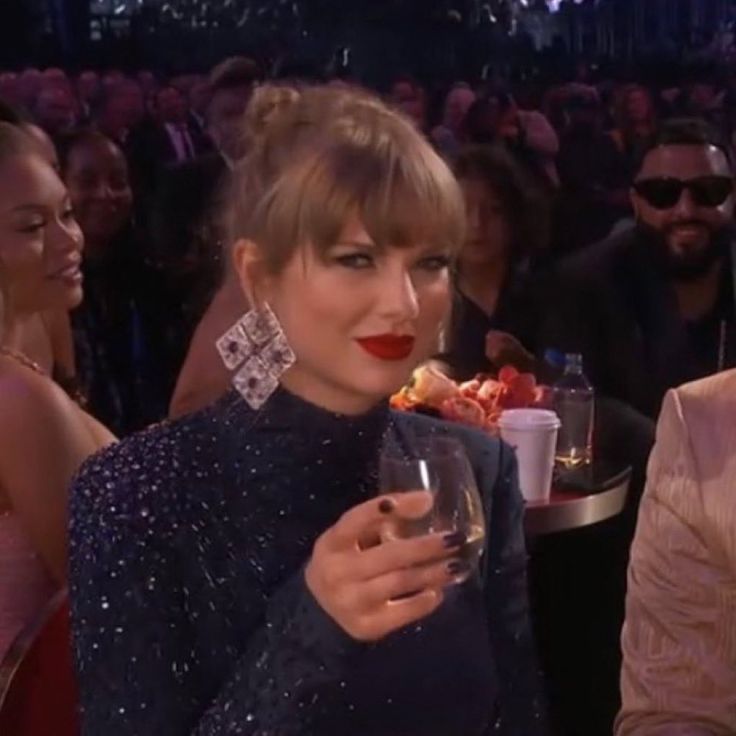 two women sitting next to each other holding wine glasses in front of a group of people