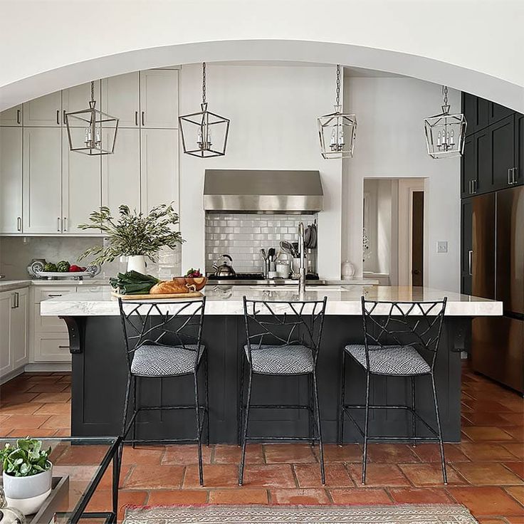 a kitchen with an island and bar stools in the center, surrounded by potted plants