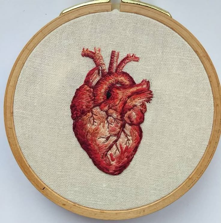 an embroidered heart is shown on a white background in a wooden frame with gold trim