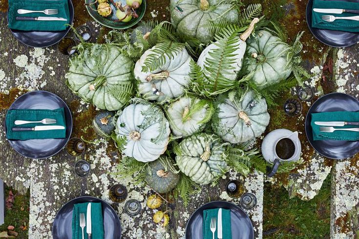 the table is set with plates, silverware and green napkins on mossy ground