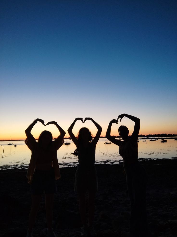 three people making heart shapes with their hands on the beach