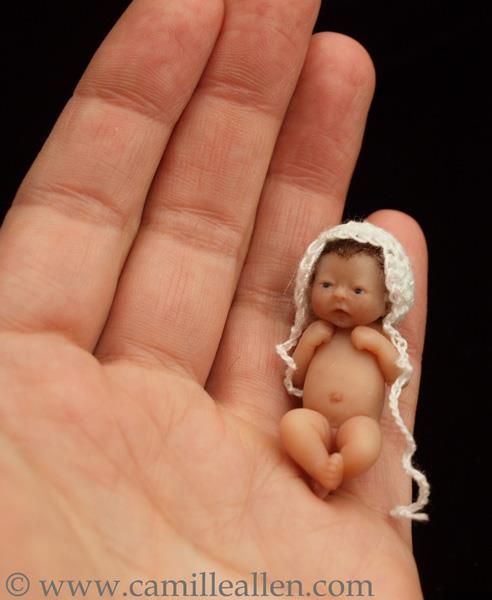 a tiny baby doll sitting in the palm of someone's hand, wearing a bonnet