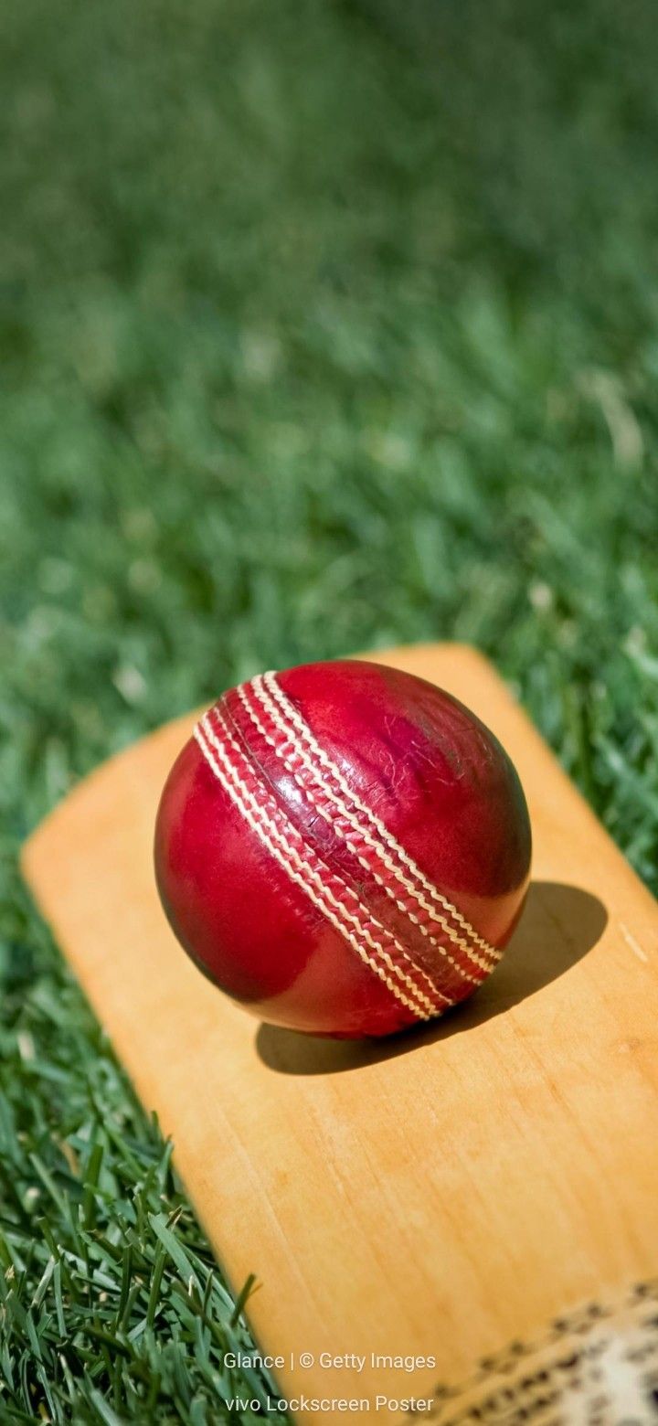 a red cricket ball sitting on top of a wooden board