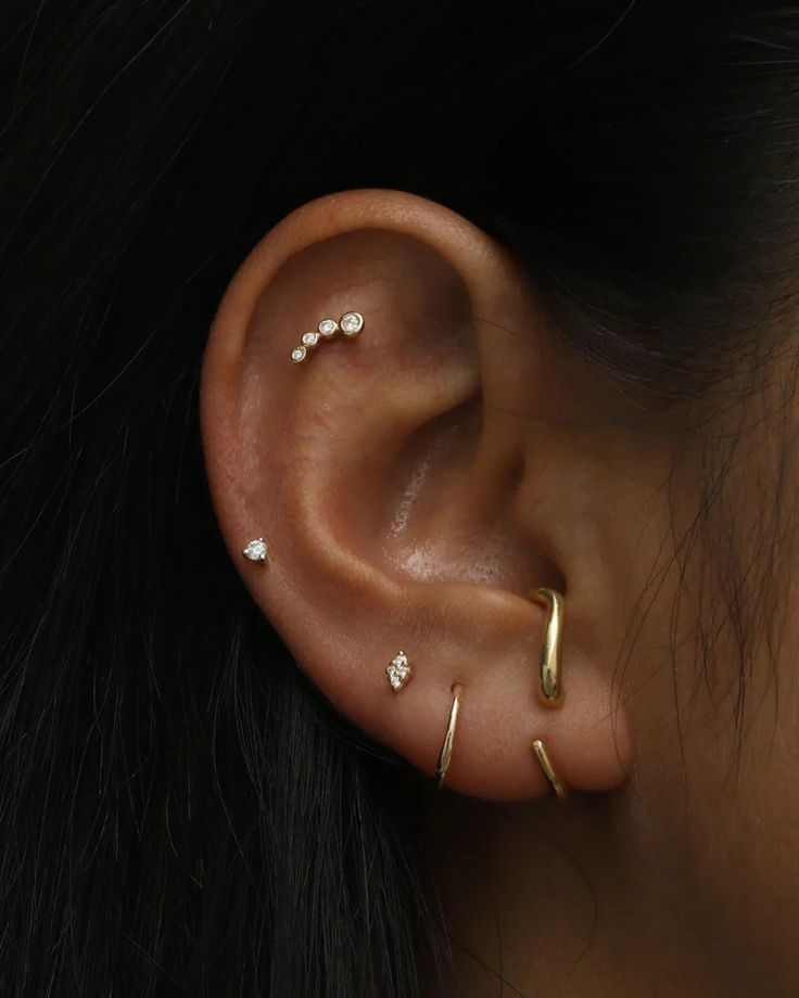 a woman wearing gold ear piercings with three small white stones on her left ear