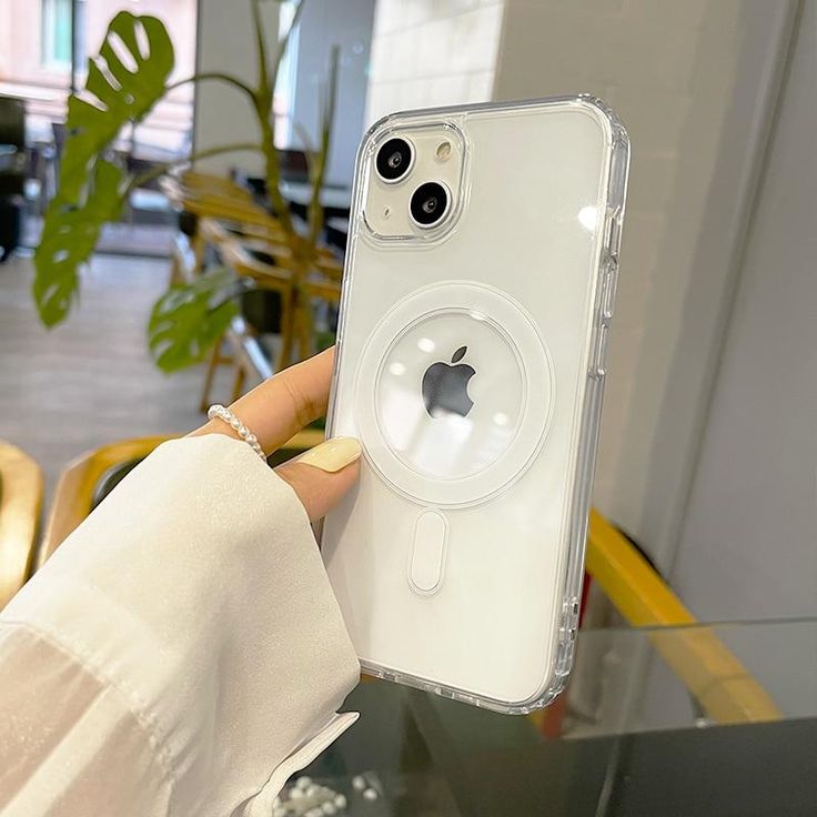 a person holding up an iphone case in front of a table with chairs and plants