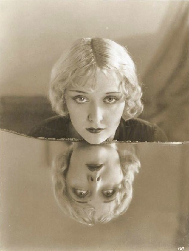 an old photo of a woman with her face reflected in the mirror, looking at herself