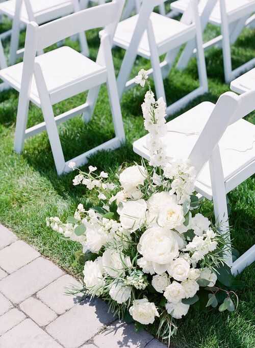 a bouquet of white flowers sitting on top of a grass covered field next to chairs