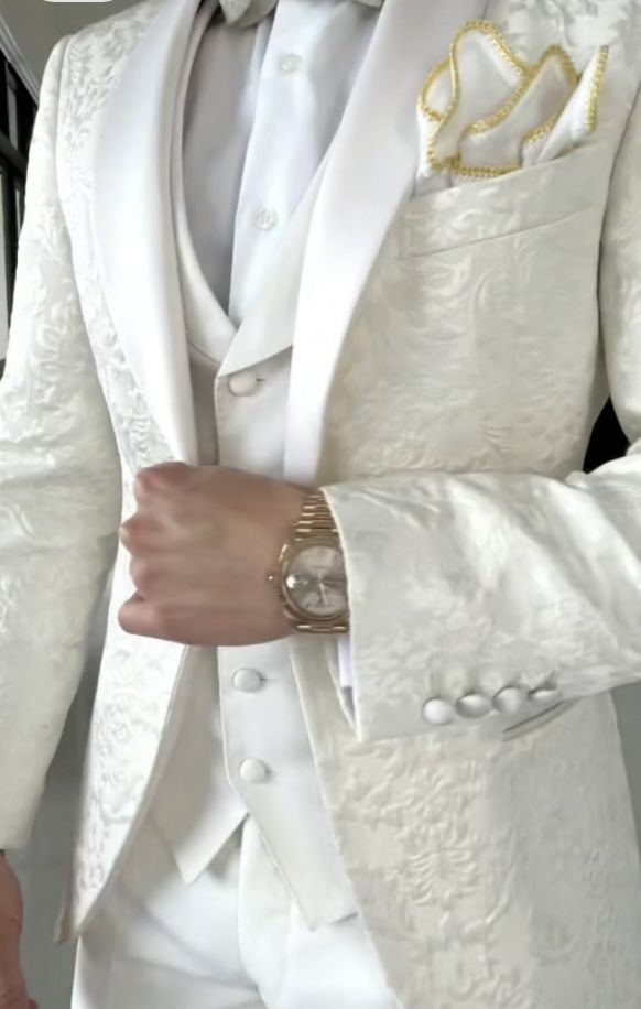 a man in a white tuxedo is holding his hand on his hip and wearing a watch