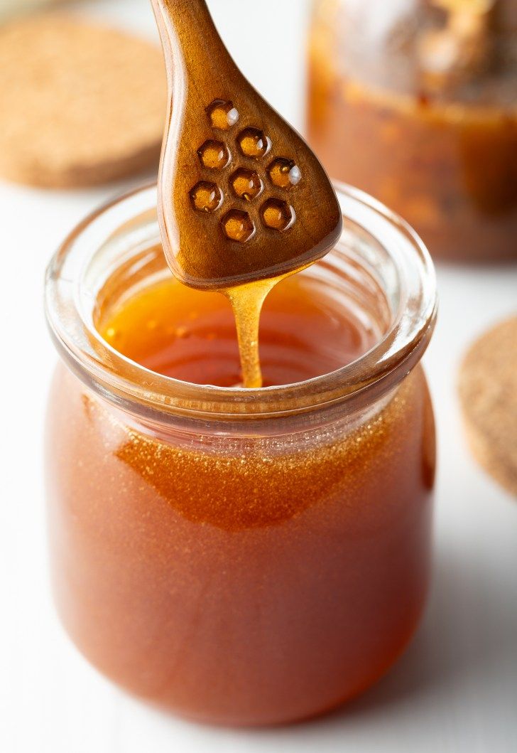 a spoon full of honey sitting in a jar next to some crackers and cookies