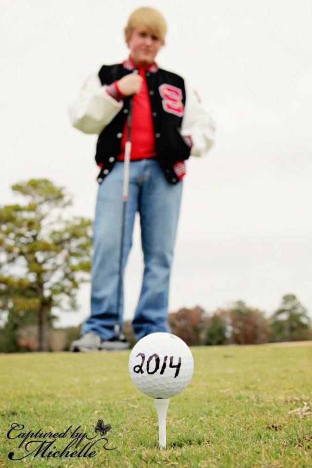 a young man standing next to a golf ball on top of a green grass covered field