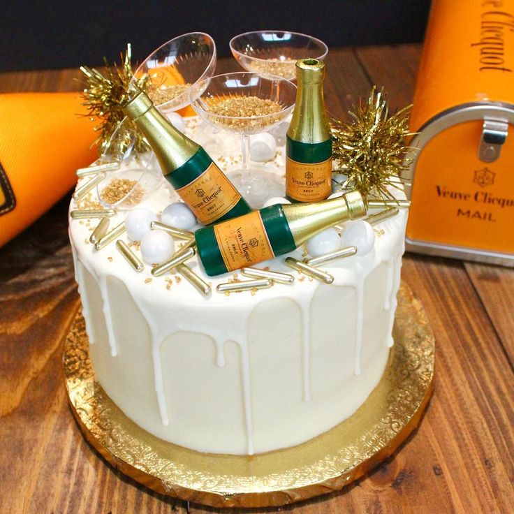 a white cake with gold decorations and champagne bottles on top, sitting on a wooden table