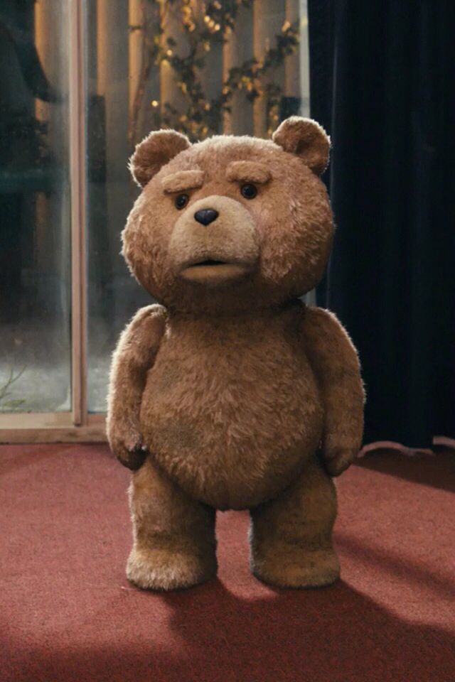 a large brown teddy bear standing on top of a red carpet next to a window