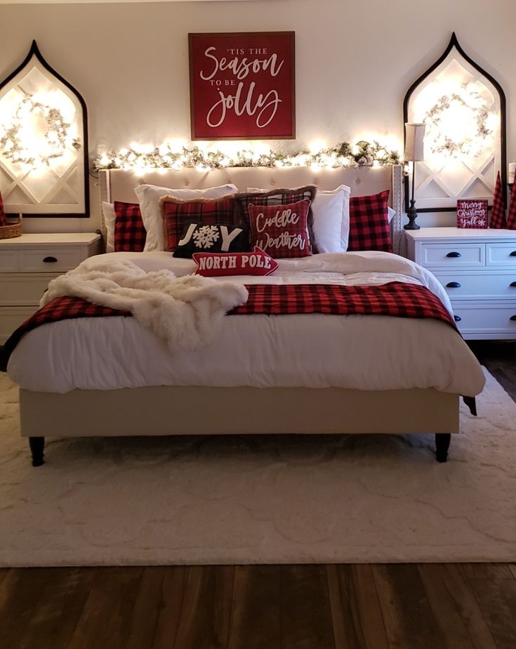 a white bed with red and black pillows on top of it next to two dressers