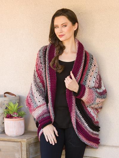 a woman standing in front of a wall wearing a pink and black knitted shawl