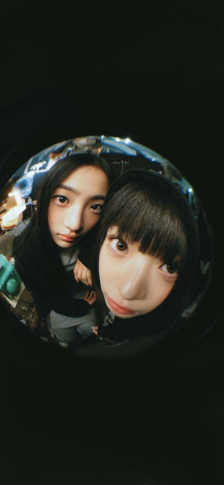 two young women are seen through the reflection of their faces in a circular object that looks like they're looking at something