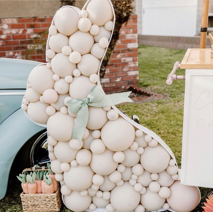 a large balloon bunny sitting on top of a table next to a blue car and flowers