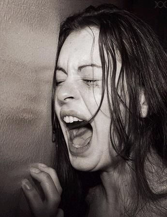 a woman with her mouth open and eyes closed, holding something in her hand while she is screaming