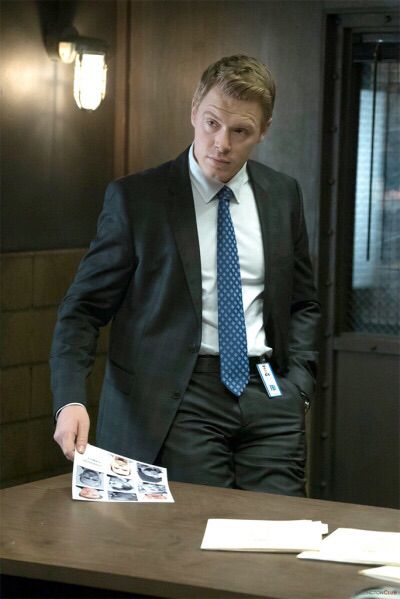 a man wearing a suit and tie standing in front of a table with papers on it