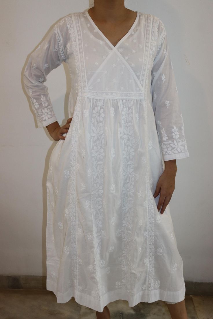 Discover timeless elegance in our pure cotton white dress, featuring a chic overlap neck, full sleeves, and convenient pockets. Adorned with exquisite vintage chikankari embroidery, this piece seamlessly blends tradition with modern style. Flows down to a Length of 48 inches Full Sleeves. Side Pockets. No side slits Machine wash and Line dry with light iron for best results.  Available in White.  Sizes : S - fits bust 34 M - fits bust 36 L - fits bust 38 XL - fits bust 40 0X - fits bust 42 1X - fits bust 44 Prewashed. Preshrunk. Traditional Long Sleeve Cutwork Dresses, Traditional Cotton Dress With Cutwork, Traditional Cotton Cutwork Dresses, Festive Long Sleeve Cutwork Dresses, White Cutwork Dress For Eid, Long White Dress With Chikankari Embroidery, White Long Dress With Chikankari Embroidery, White Cutwork Dress For Festive Occasions, Festive White Dress With Cutwork