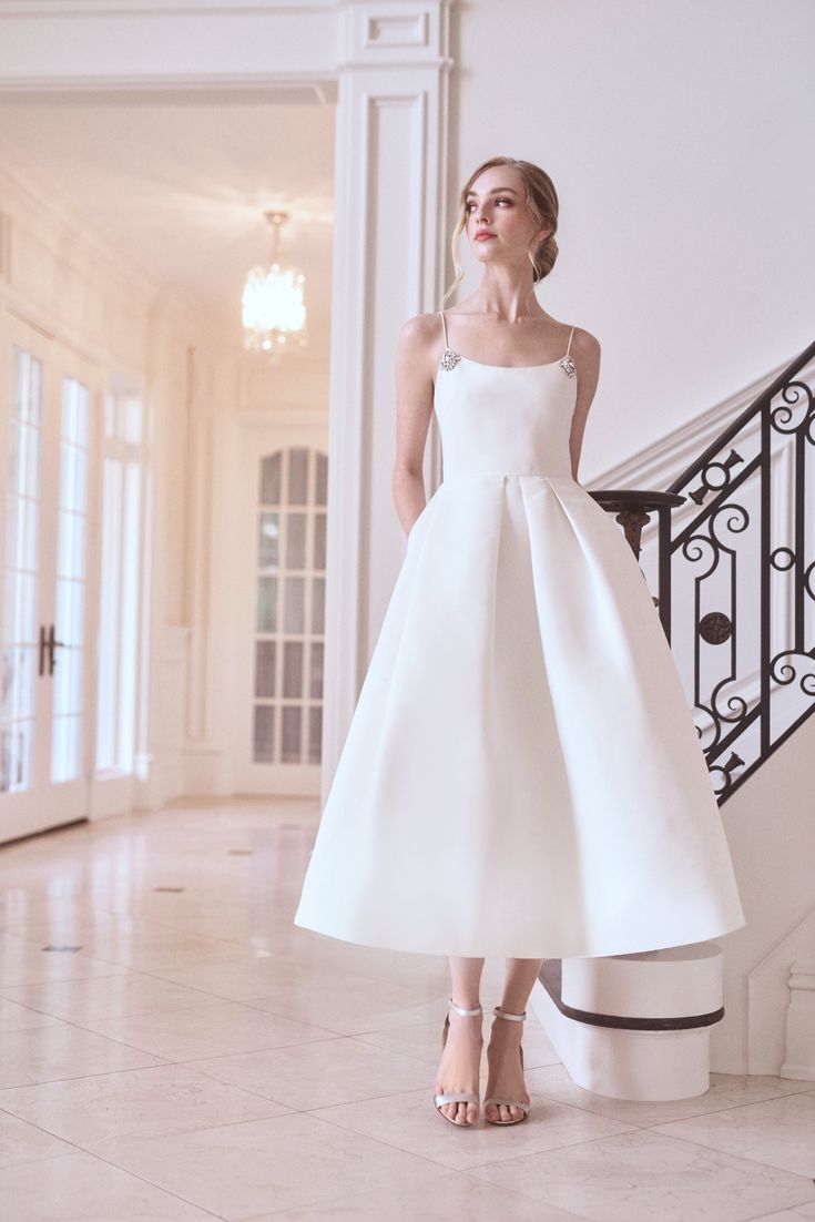 a woman in a white dress standing next to a stair case and looking off into the distance