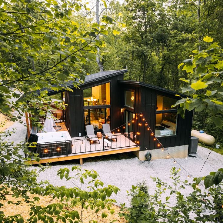 a small black cabin in the woods with hot tub