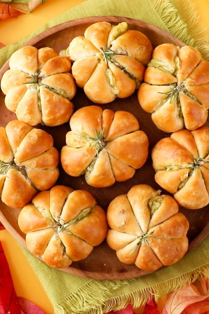 a wooden plate topped with rolls on top of a green cloth next to autumn leaves