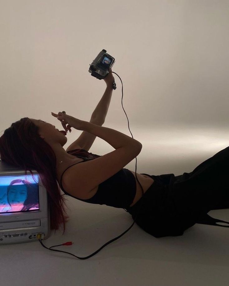 a woman laying on the ground with a camera in her hand and a television behind her