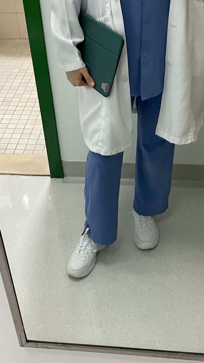 a person in white lab coat and blue pants holding a green folder while standing next to a door