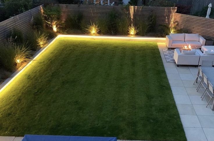 a large backyard with lawn and seating area at night, lit up by outdoor lighting