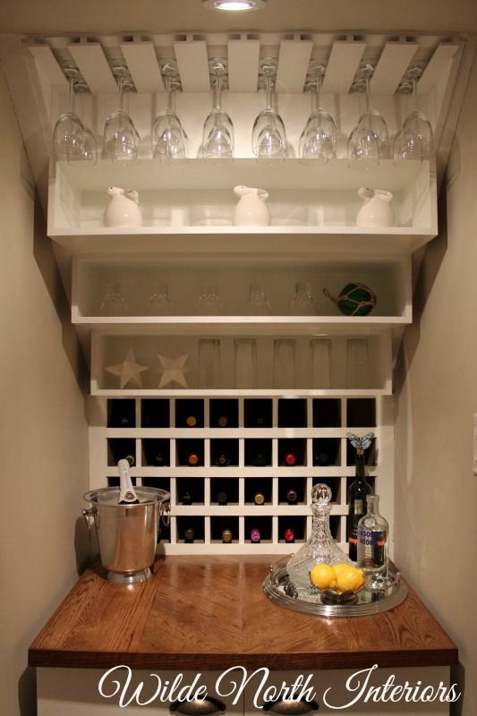 a kitchen counter with wine glasses on the top and bottom shelf above it that is filled with bottles