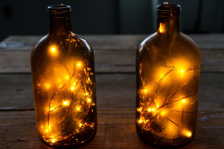 two glass bottles with lights in them sitting on a wooden table next to each other