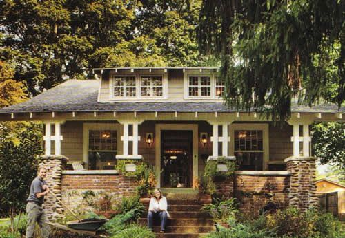 two people are sitting on the steps in front of a house with trees and bushes