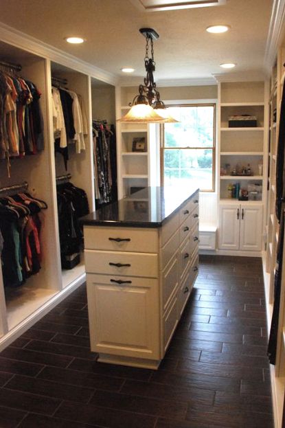 a walk in closet with white cabinets and black counter tops, along with dark tile flooring