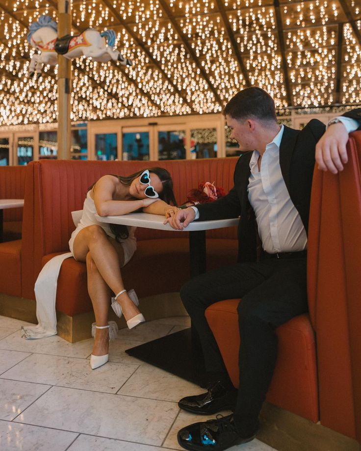 a man and woman sitting at a table in a restaurant with lights on the ceiling