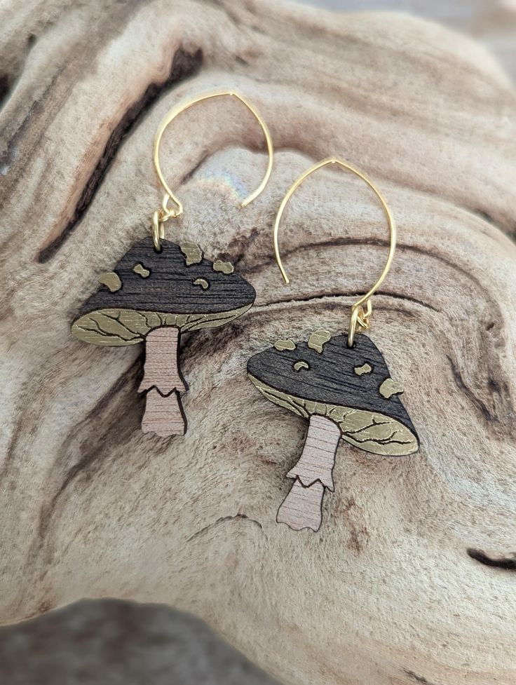 Toadstool inspired wood mushroom earrings, featuring ebony wood stain on mushroom caps with metallic gold spots and undersides, over light cherry stained stalks. Backs are not etched. Earrings hang from gold plated, nickel free hooks.  Please note that clear stoppers on hooks are for shipping stability and do not need to be worn with earrings. Ebony Wood Stain, Mushroom Caps, Cherry Stain, Mushroom Earrings, Stuffed Mushroom Caps, Wood Stain, Ebony Wood, Metallic Gold, Staining Wood