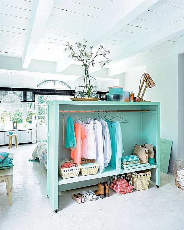 a room filled with lots of clothes and baskets on top of a blue shelf next to a window