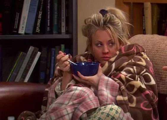 a woman sitting on a couch holding a bowl in her hand and looking at the camera