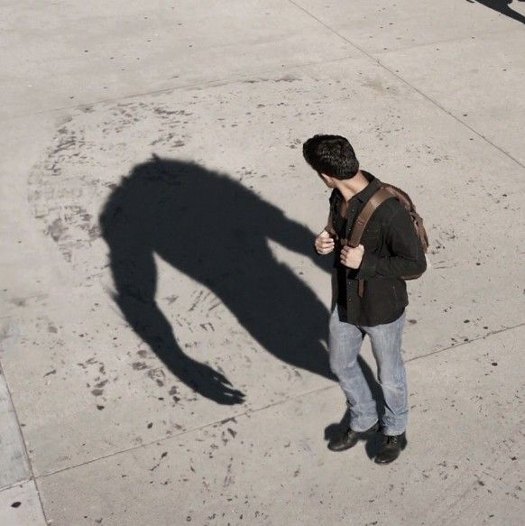 a man standing on the sidewalk looking at his cell phone and casting a long shadow