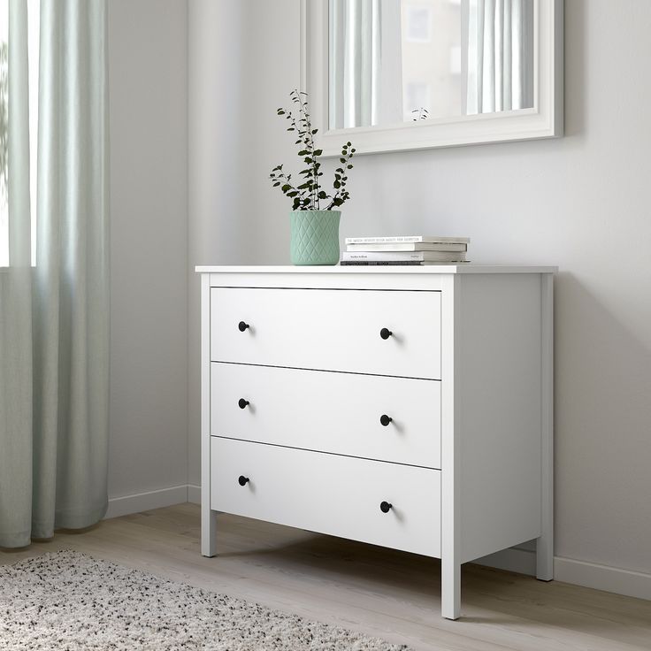 a white dresser with two drawers and a mirror on the wall above it in a room