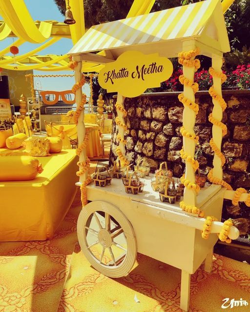 an outdoor dessert cart is decorated with yellow and white flowers, lemon garlands, and cupcakes