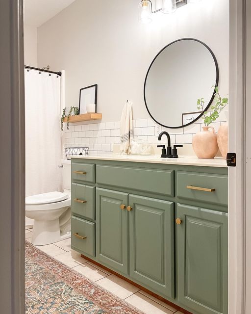 a bathroom with green cabinets and a round mirror on the wall above the sink, along with a rug