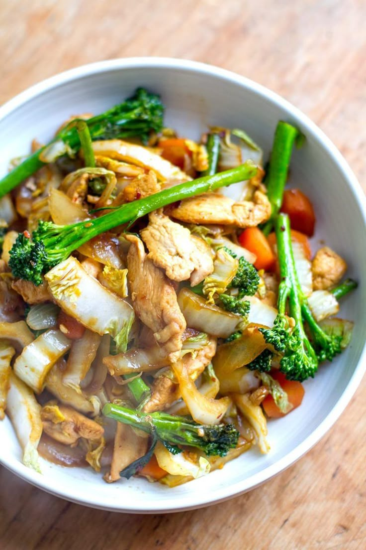 a white bowl filled with meat and veggies on top of a wooden table